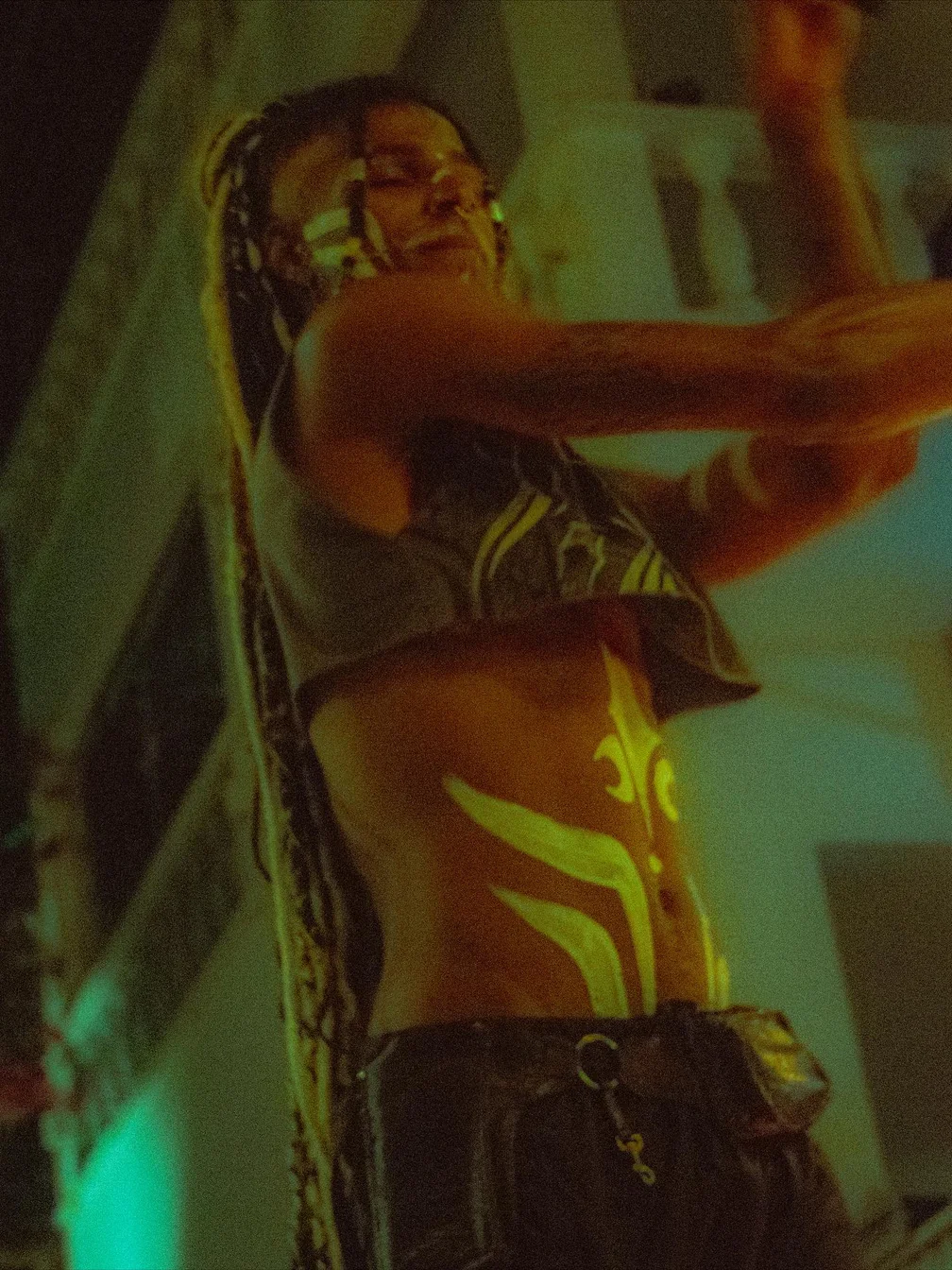 Dança sob luz verde e quente, com pintura corporal neon