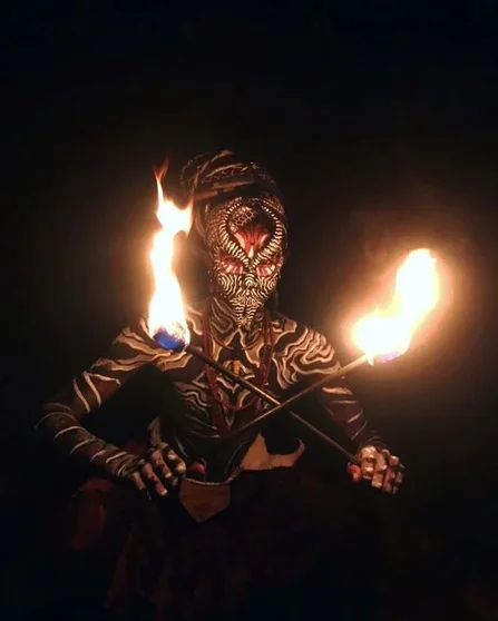 Performance de pirofagia à noite, com máscara e chamas nas mãos